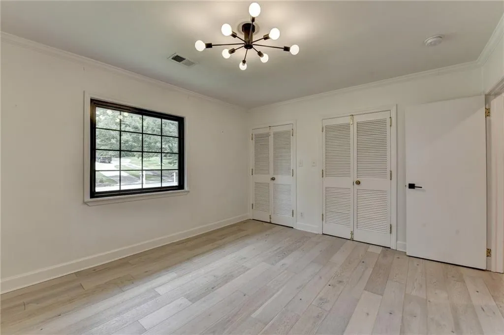 Unfurnished bedroom with two closets, a chandelier, crown molding, and light wood finished floors