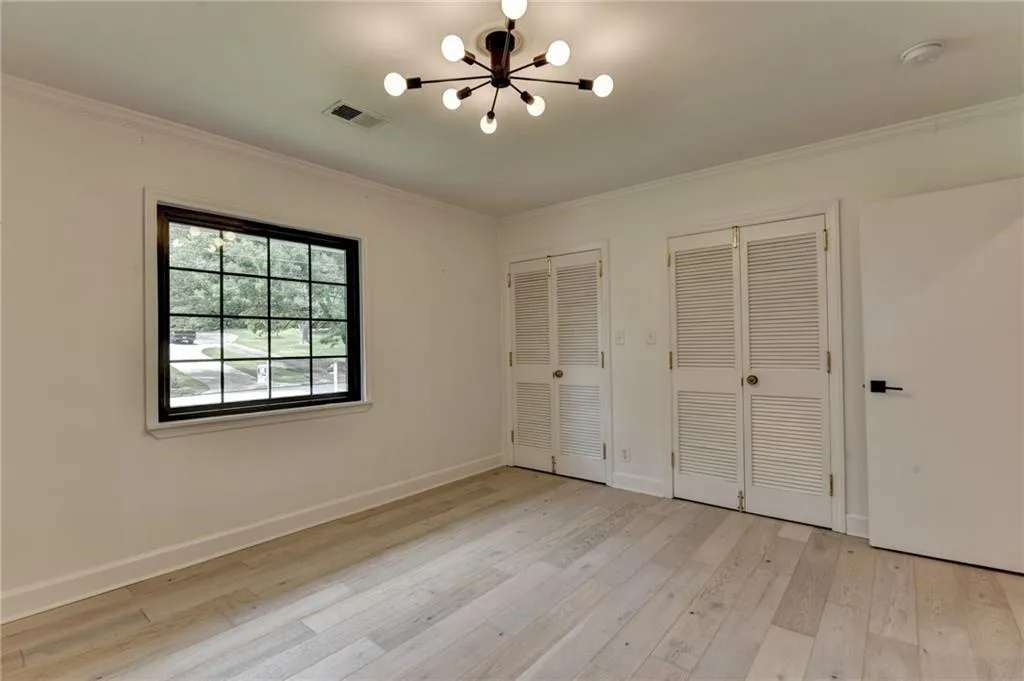 Unfurnished bedroom with multiple closets, a chandelier, light wood-type flooring, and ornamental molding