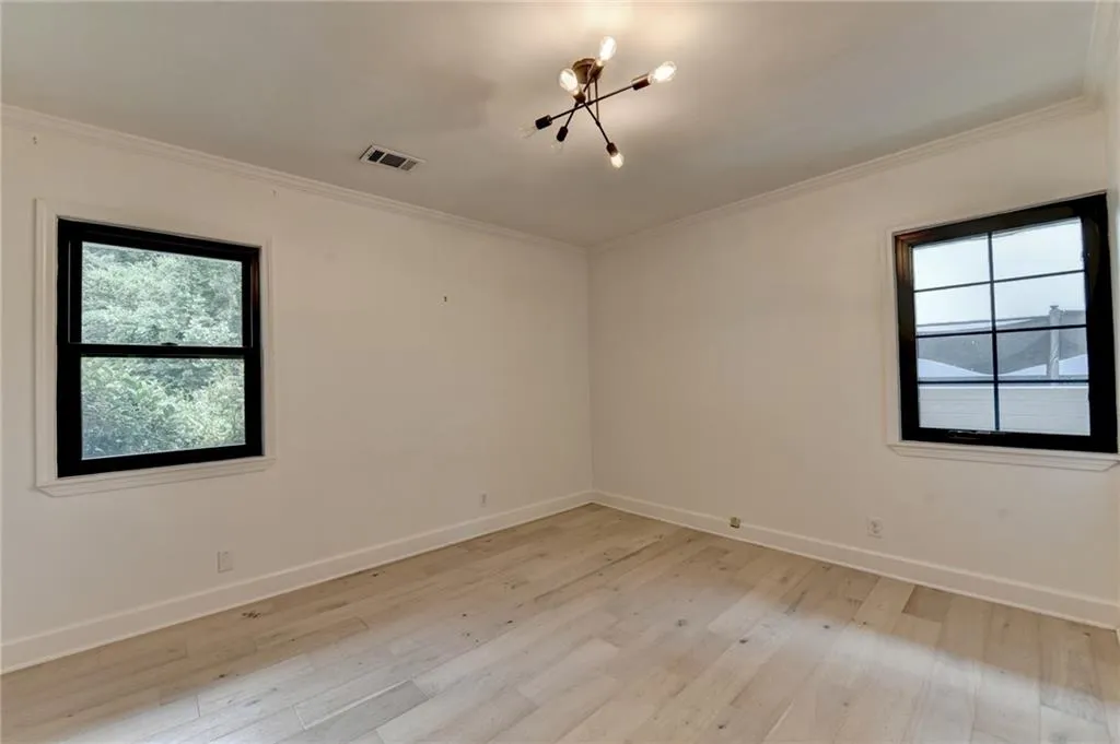 Unfurnished room with a chandelier, light wood finished floors, and ornamental molding