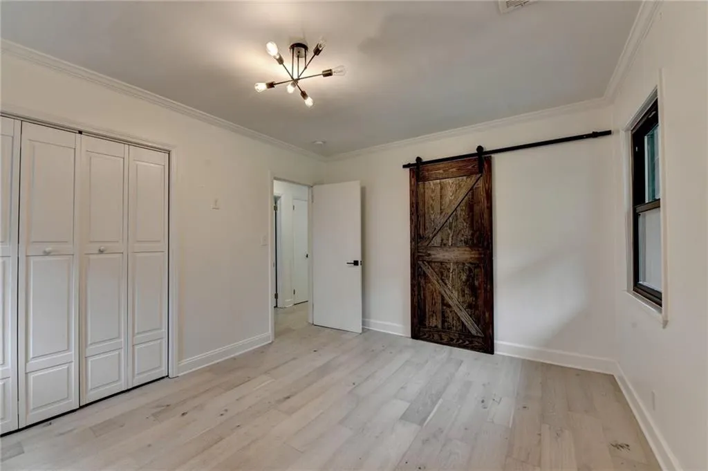 Unfurnished bedroom with a chandelier, light wood-style floors, crown molding, a barn door, and a closet