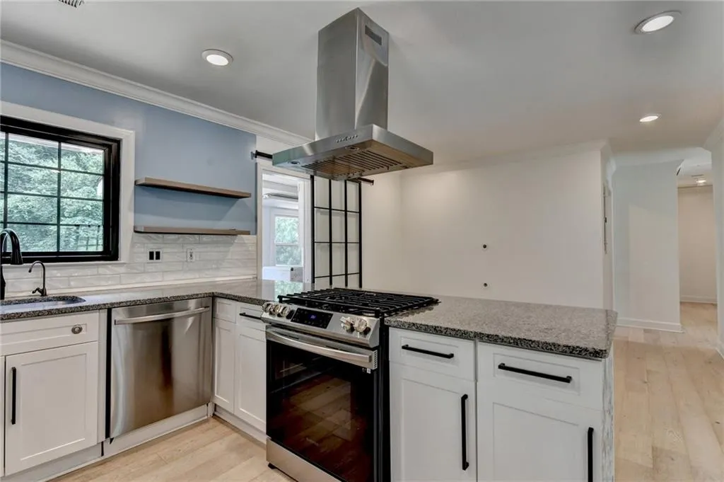 Kitchen with stainless steel appliances, range hood, a peninsula, crown molding, and light wood-type flooring