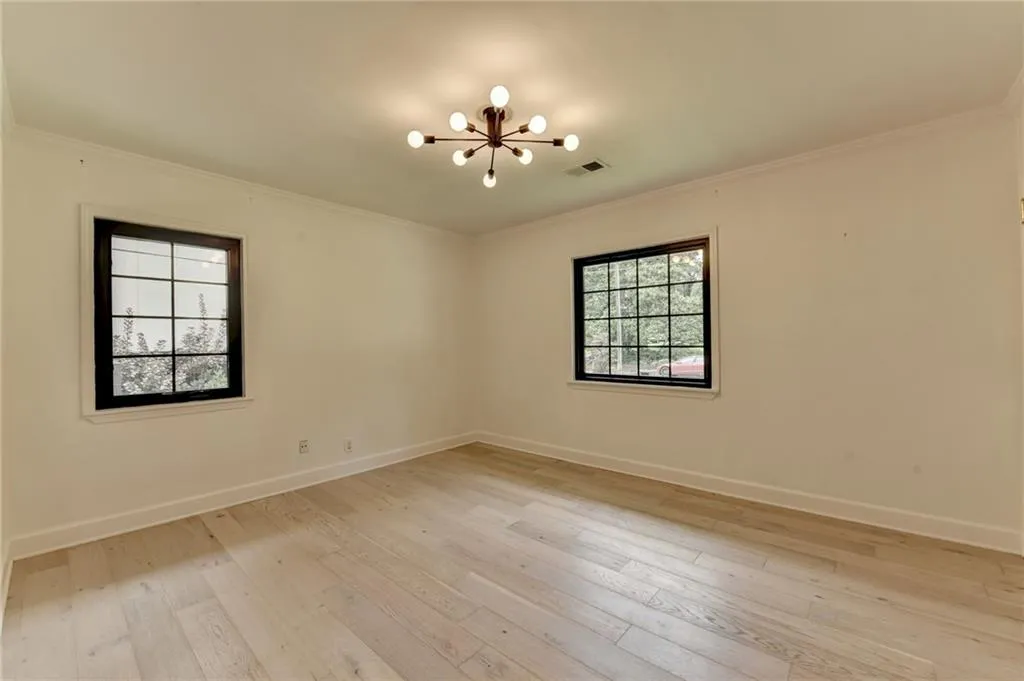 Unfurnished room featuring a chandelier, crown molding, and light wood-style floors