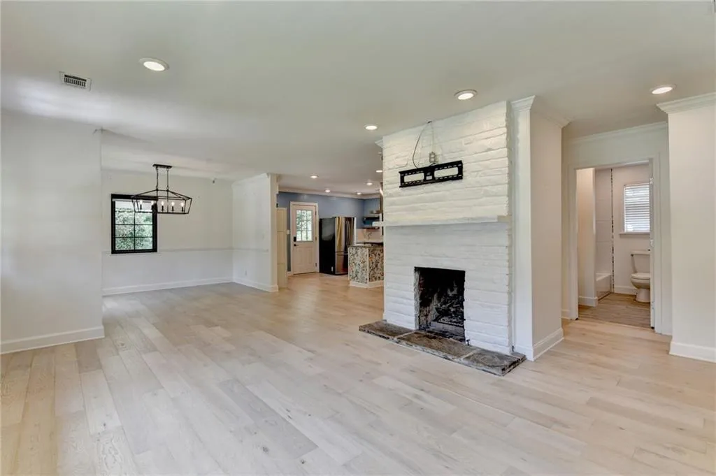 Unfurnished living room with crown molding, a fireplace, light wood finished floors, a chandelier, and recessed lighting