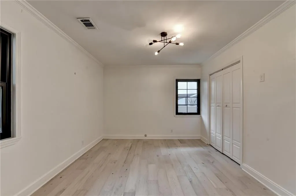 Unfurnished bedroom featuring a chandelier, light wood-style flooring, crown molding, and a closet