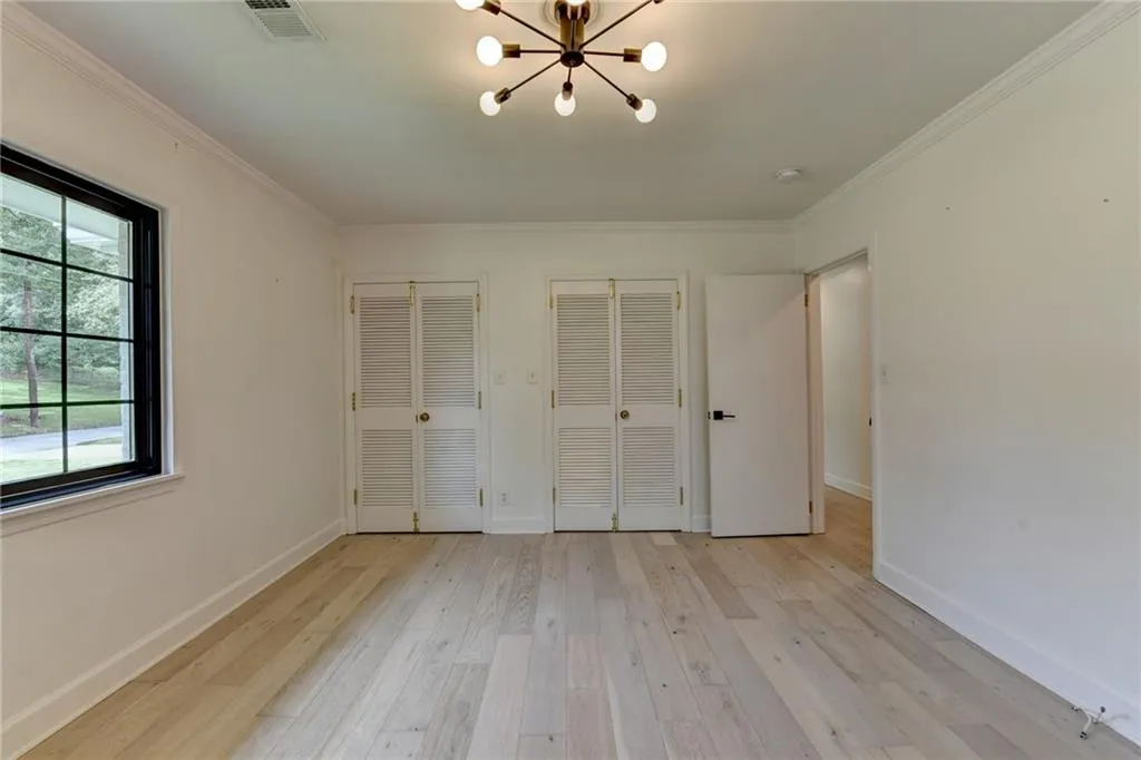 Unfurnished bedroom featuring two closets, a chandelier, light wood finished floors, and crown molding