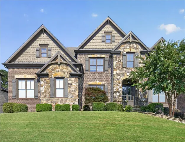 Stone and brick facade featuring multiple gables, shuttered windows, and a mature tree
