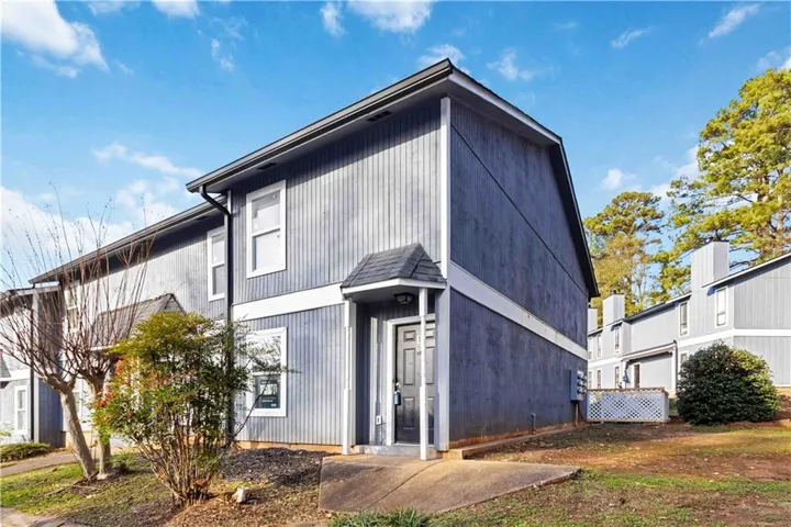Wood-sided townhouse exterior with a covered entry, multiple windows, and a mature tree backdrop