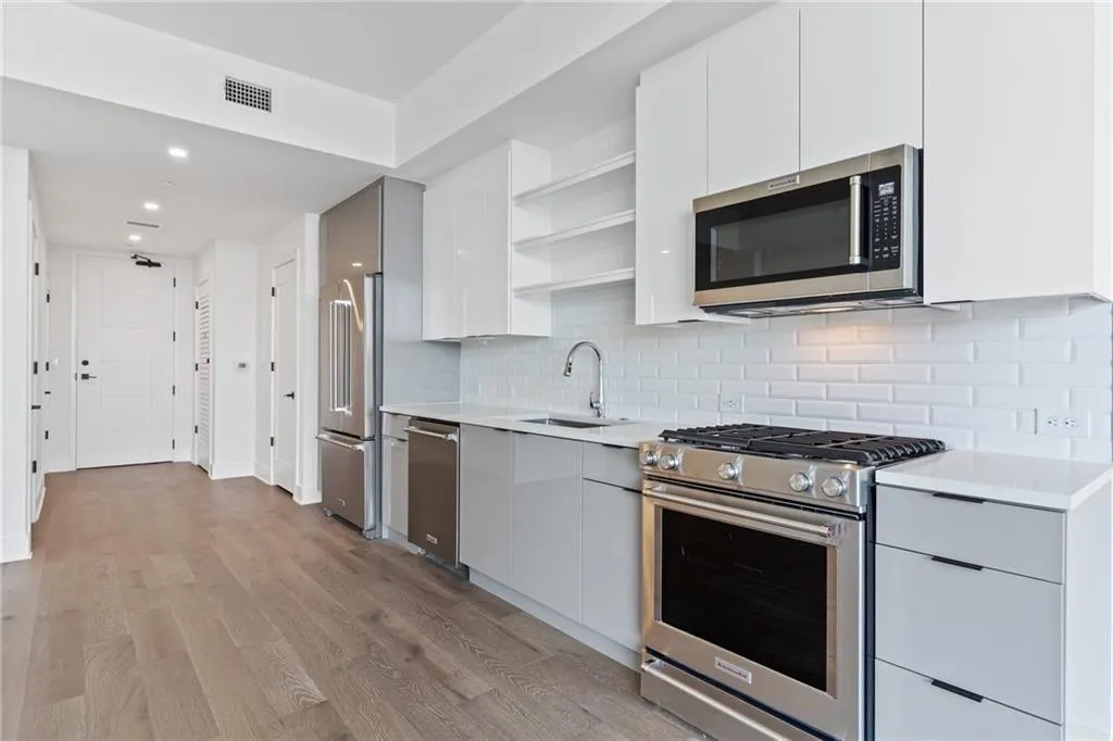 Kitchen with modern cabinets, high quality appliances, open shelves, light countertops, and light wood-style floors