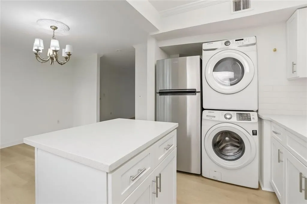 Washroom with light wood finished floors, a chandelier, and stacked washer and clothes dryer