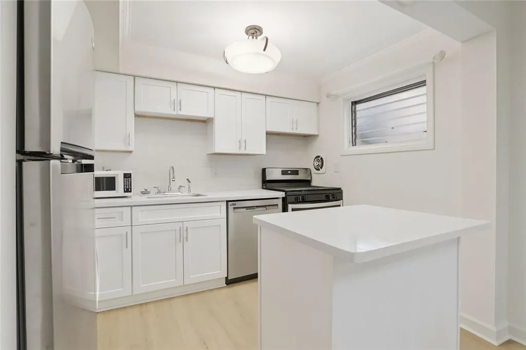 Kitchen with white cabinetry, stainless steel appliances, tasteful backsplash, light wood-style floors, and a center island