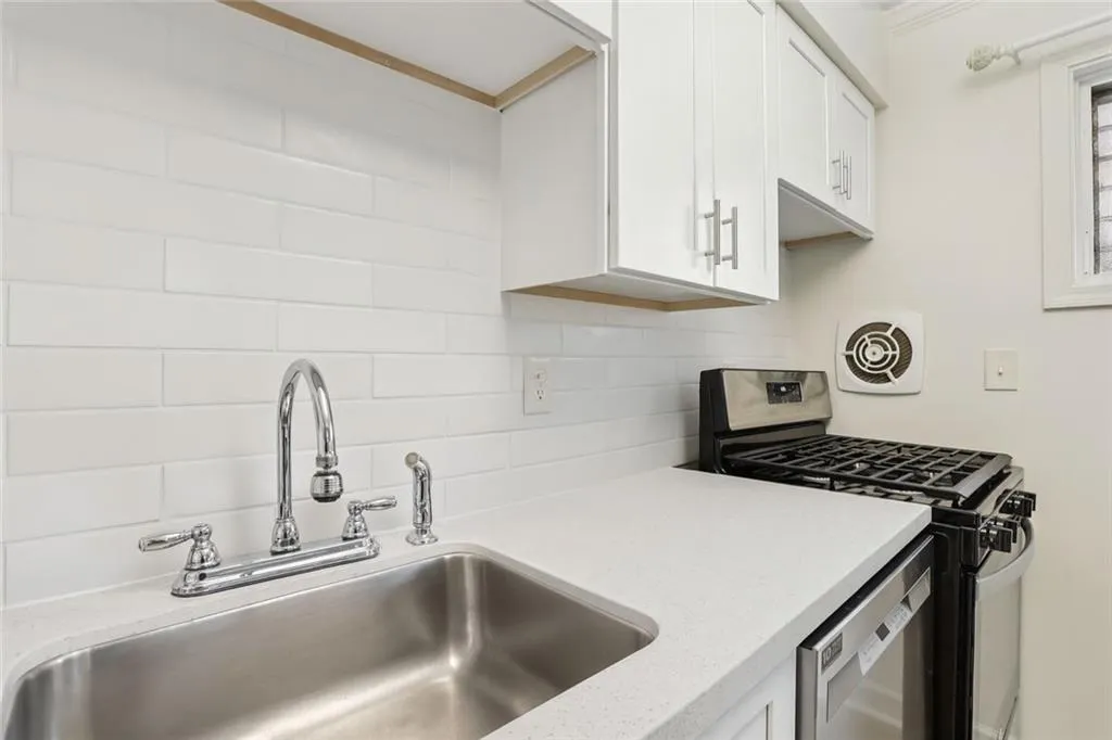 Kitchen featuring stainless steel appliances, white cabinetry, light stone counters, and backsplash