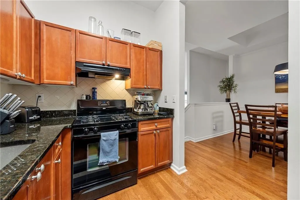 Kitchen featuring black gas stove, tasteful backsplash, dark stone counters, under cabinet range hood, and light wood-style floors