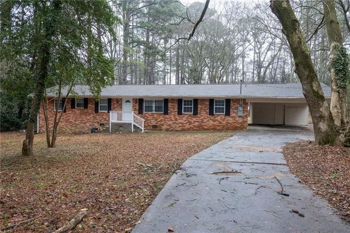 Brick ranch-style residence featuring a covered front entry with white railings, black window shutters, a paved driveway, and an attached carport