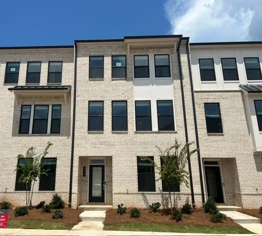 Three-story brick facade, black frame windows, front entry with transom window, accent siding, and landscaping
