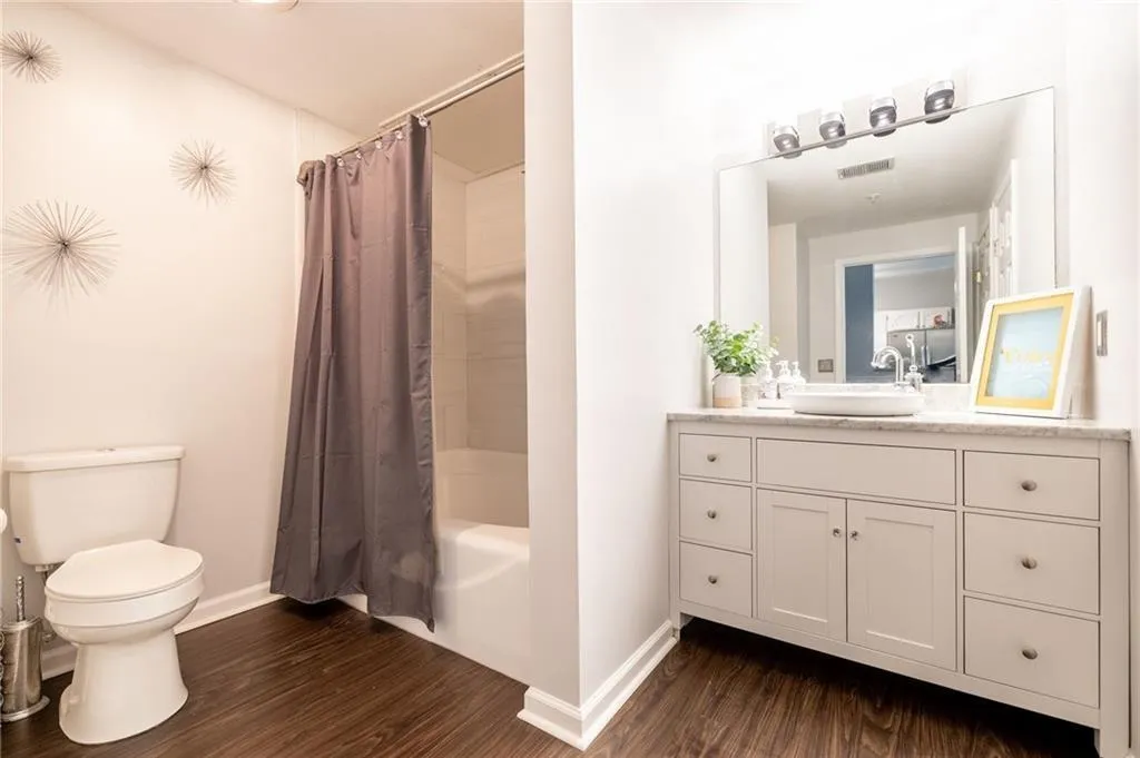 Full bathroom featuring baseboards, wood finished floors, toilet, vanity, and shower / tub combo with curtain
