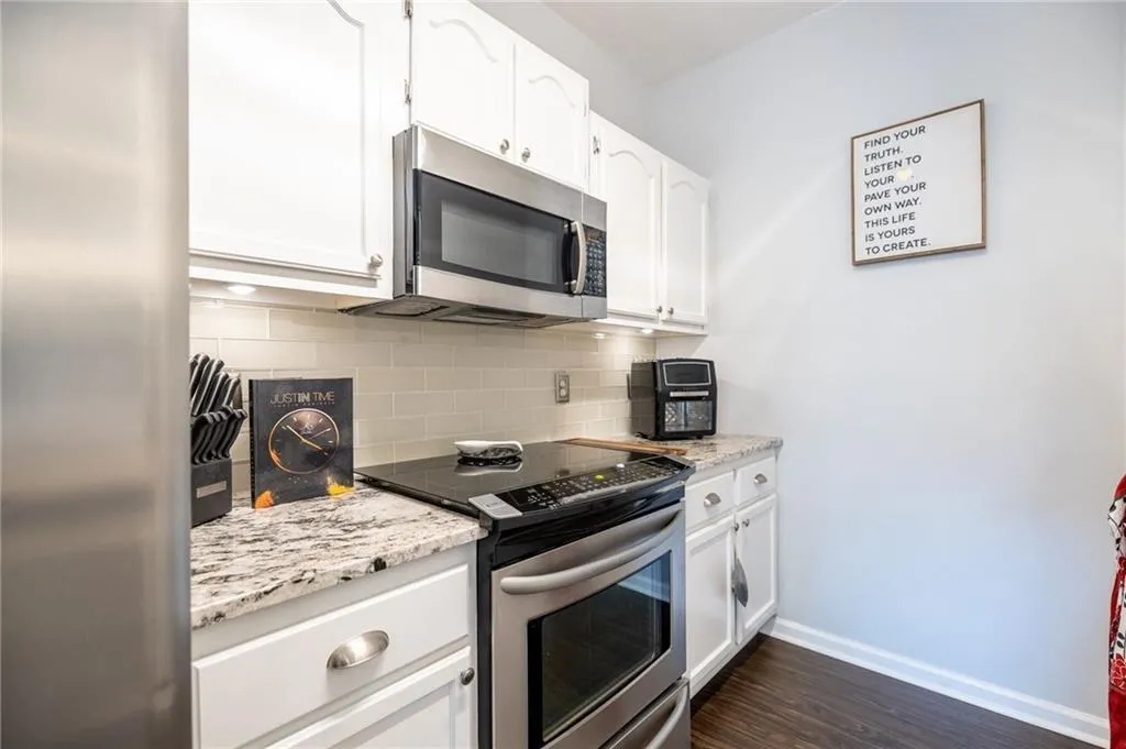 Kitchen with appliances with stainless steel finishes, baseboards, dark wood-style floors, white cabinetry, and tasteful backsplash