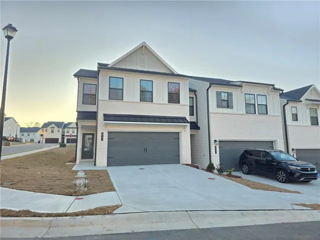 Contemporary townhome exterior featuring white siding and brick, black framed windows, a two-car garage, and an asphalt shingle roof