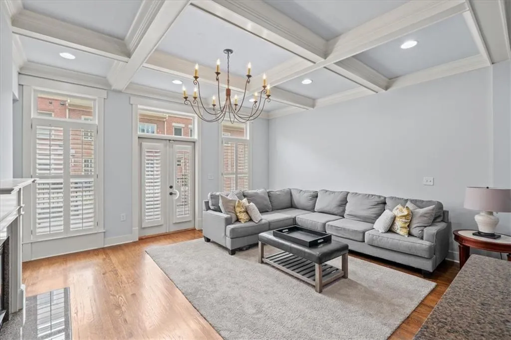 Living room featuring a high end fireplace, beam ceiling, wood finished floors, a chandelier, and french doors