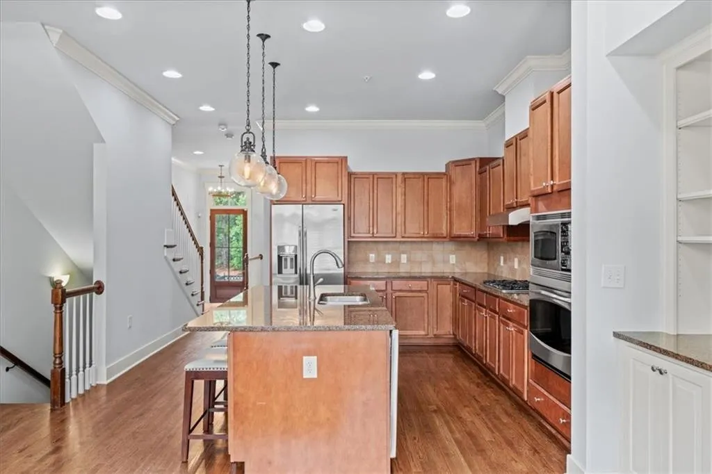 Kitchen with ornamental molding, brown cabinetry, backsplash, dark stone counters, and hanging light fixtures