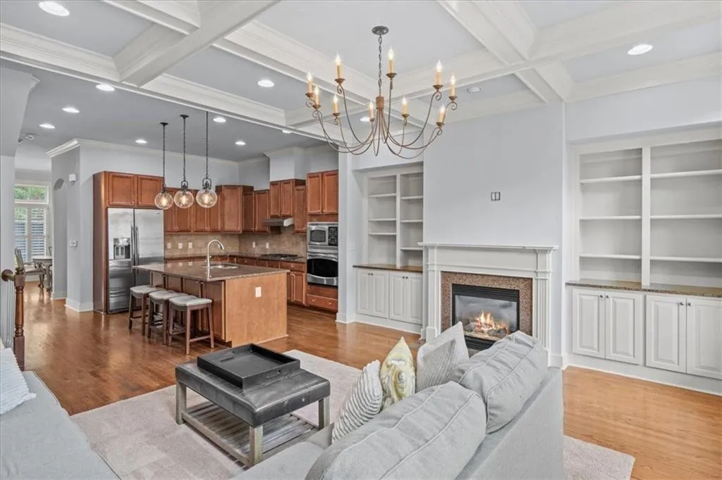 Living room featuring beam ceiling, light wood finished floors, coffered ceiling, a glass covered fireplace, and a chandelier
