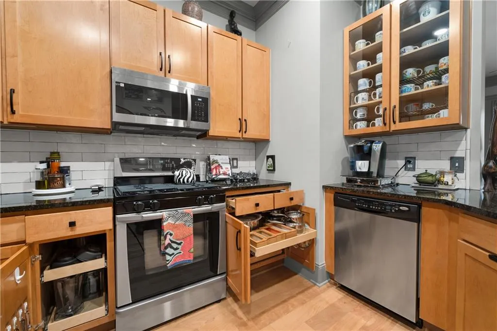 Kitchen featuring appliances with stainless steel finishes, ornamental molding, decorative backsplash, light wood-type flooring, and dark stone counters
