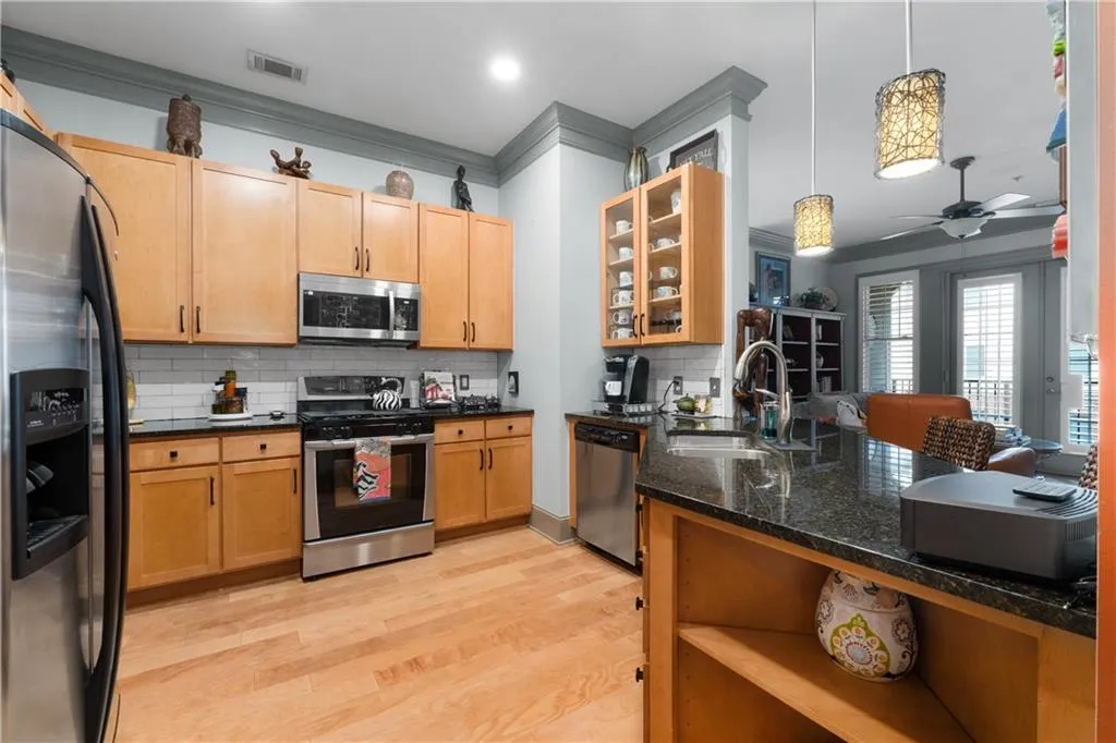 Kitchen with appliances with stainless steel finishes, backsplash, crown molding, light wood finished floors, and pendant lighting