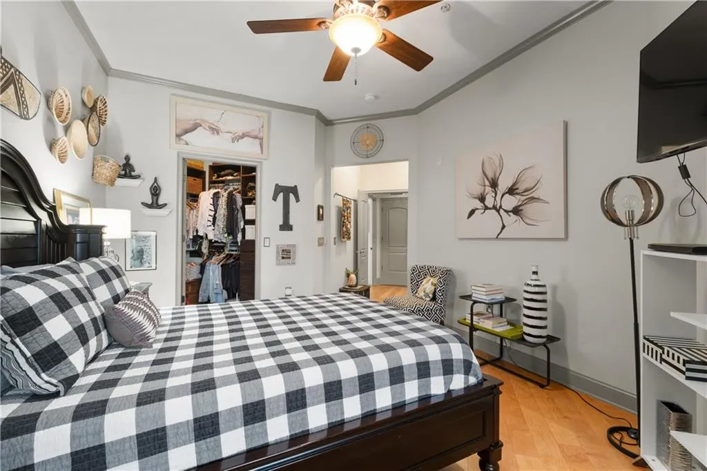 Bedroom featuring ornamental molding, light wood-type flooring, a spacious closet, and a ceiling fan