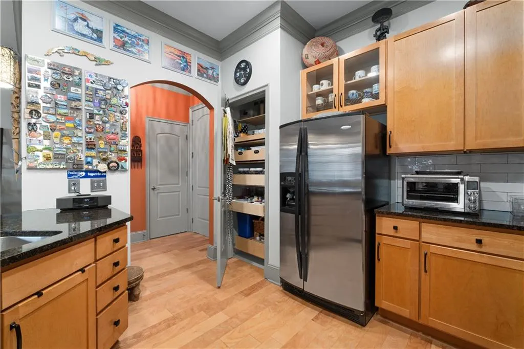 Kitchen with stainless steel fridge, arched walkways, dark stone counters, light wood finished floors, and tasteful backsplash