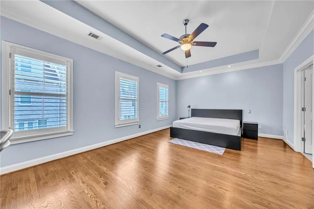 3rd level primary bedroom featuring ornamental molding, a tray ceiling, hardwood  floors, and ceiling fan
