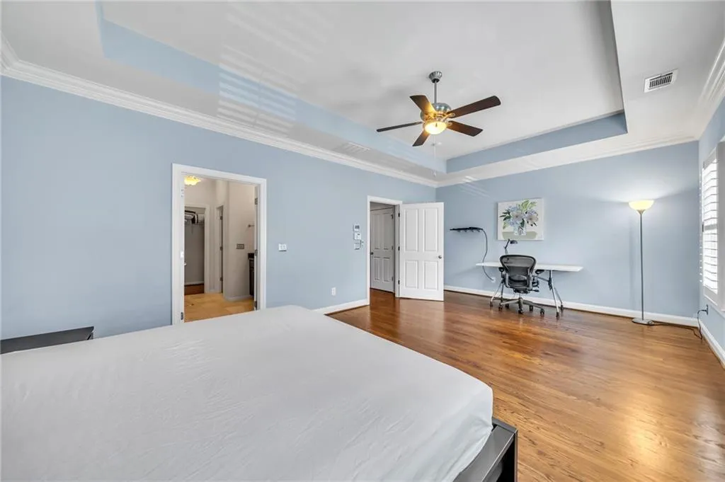 3rd level primary bedroom featuring ornamental molding, a tray ceiling, hardwood  floors, and ceiling fan