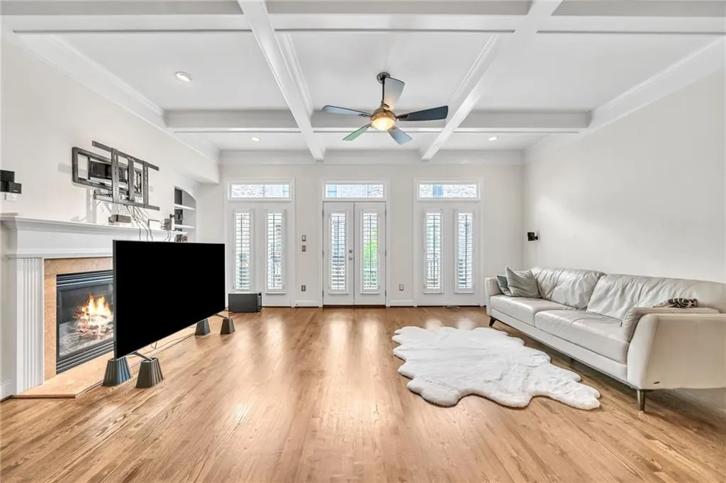 Living area featuring light wood-style floors, beam ceiling, a fireplace, coffered ceiling, and ceiling fan