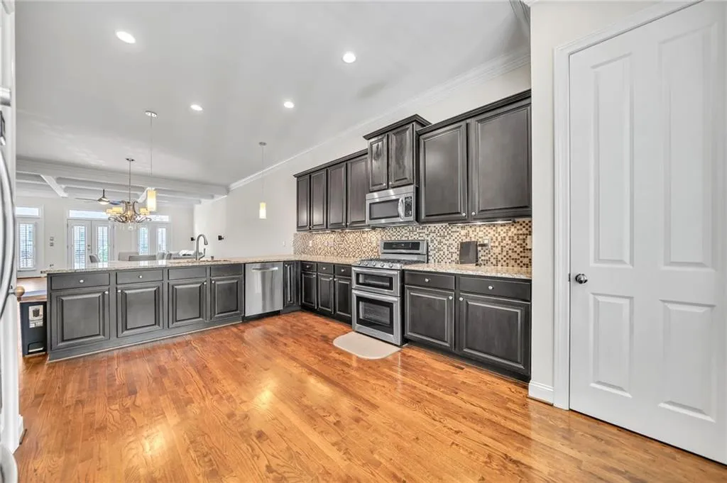 Kitchen with crown molding, pendant lighting, appliances with stainless steel finishes, light stone countertops, and a peninsula