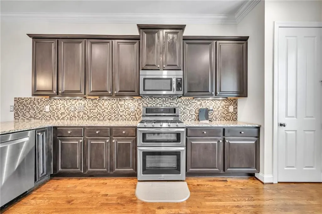 Kitchen featuring dark brown cabinetry, stainless steel appliances, light stone countertops, crown molding, and decorative backsplash