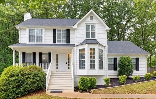 Two-story residence featuring white siding, a covered porch, bay windows, and a dark roof