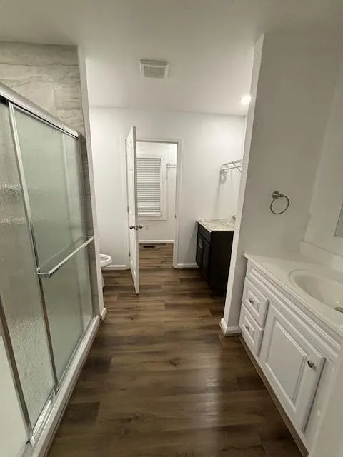 Full bathroom with two vanities, a stall shower, wood finished floors, and recessed lighting