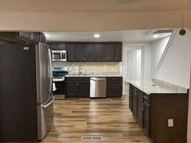 Kitchen with stainless steel appliances, wood finished floors, dark brown cabinets, tasteful backsplash, and recessed lighting