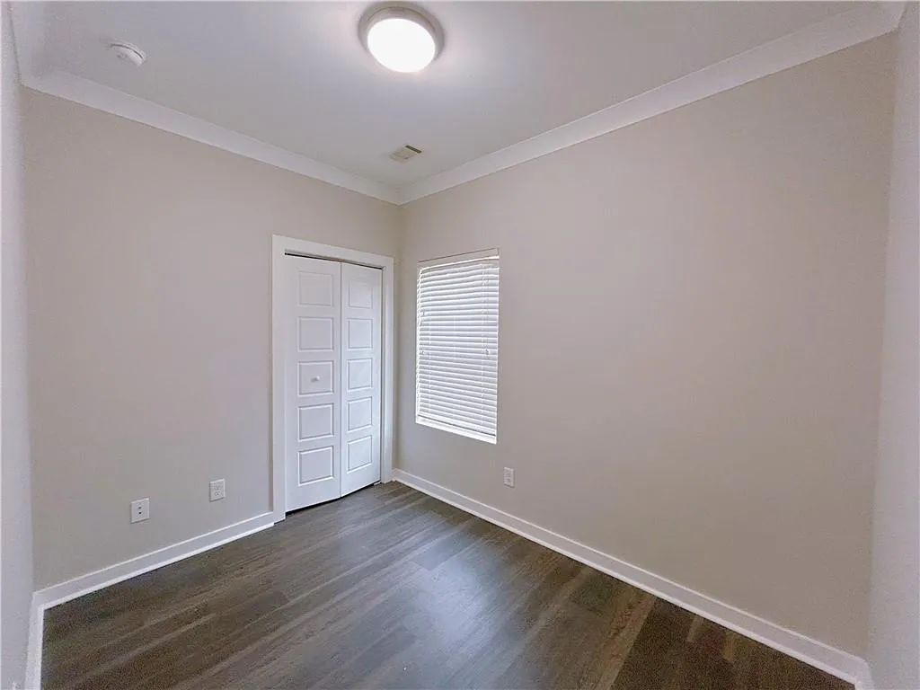 Unfurnished bedroom featuring dark hardwood / wood-style flooring, ornamental molding, and a closet