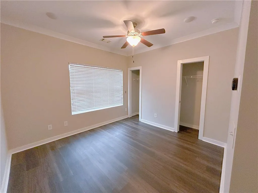 Unfurnished bedroom with ceiling fan, a closet, dark hardwood / wood-style floors, and ornamental molding