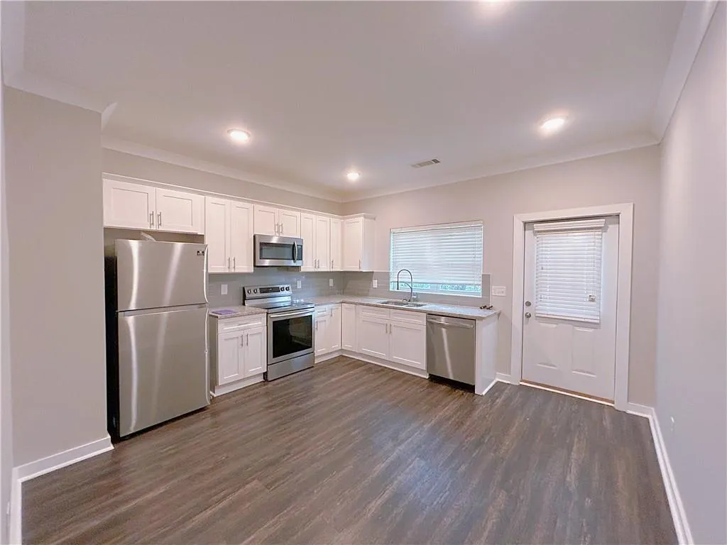 Kitchen featuring white cabinetry, sink, stainless steel appliances, dark hardwood / wood-style floors, and ornamental molding