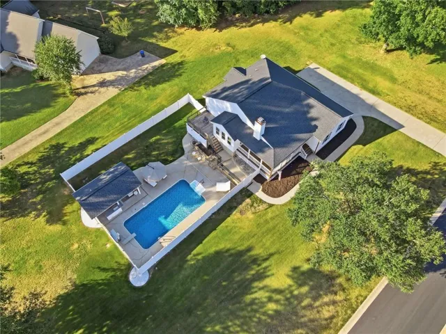 Expansive property featuring a rectangular pool, pool house, multi-level deck, paved driveway, and mature landscaping