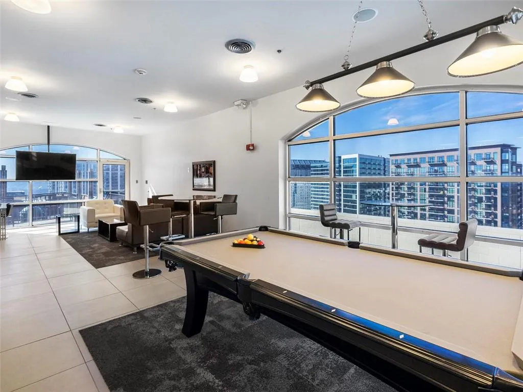 High-rise recreation space featuring a regulation pool table with pendant lighting, wall-mounted entertainment display, and extensive floor-to-ceiling windows showcasing panoramic cityscape vistas