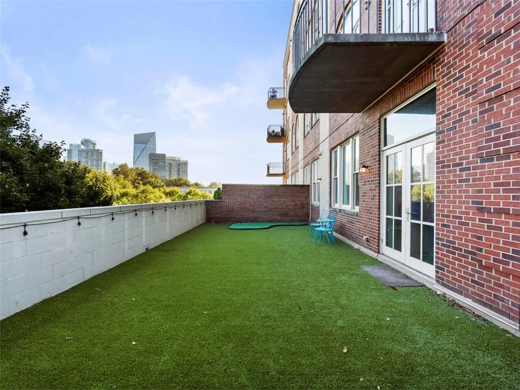 Expansive rooftop terrace with professionally installed artificial turf, white privacy fencing, and direct access via glass sliding doors from the residence