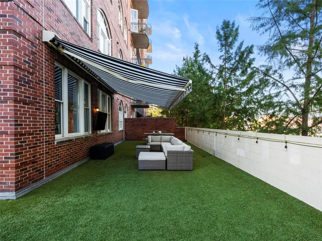 Expansive outdoor patio featuring artificial turf, a striped retractable awning, and string lighting