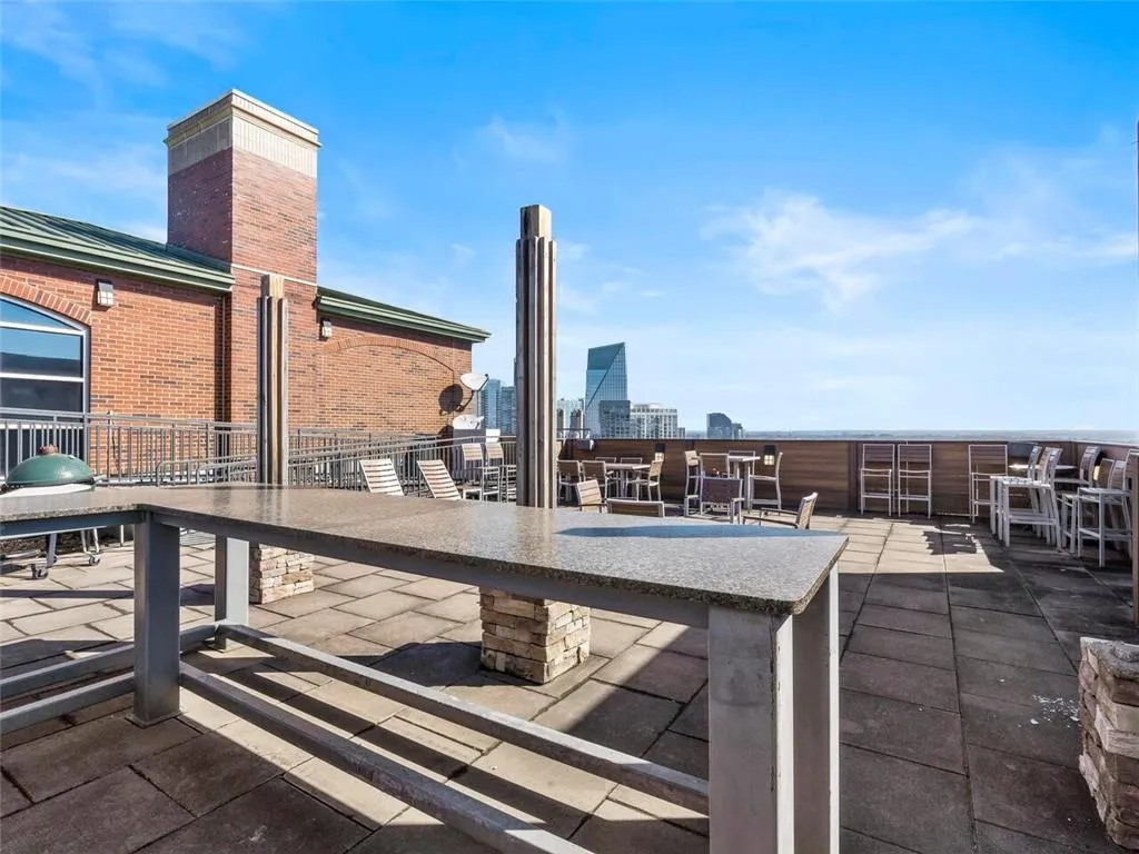 Rooftop deck featuring a stone-finish countertop, paver flooring, brick building facade, and wood-paneled perimeter