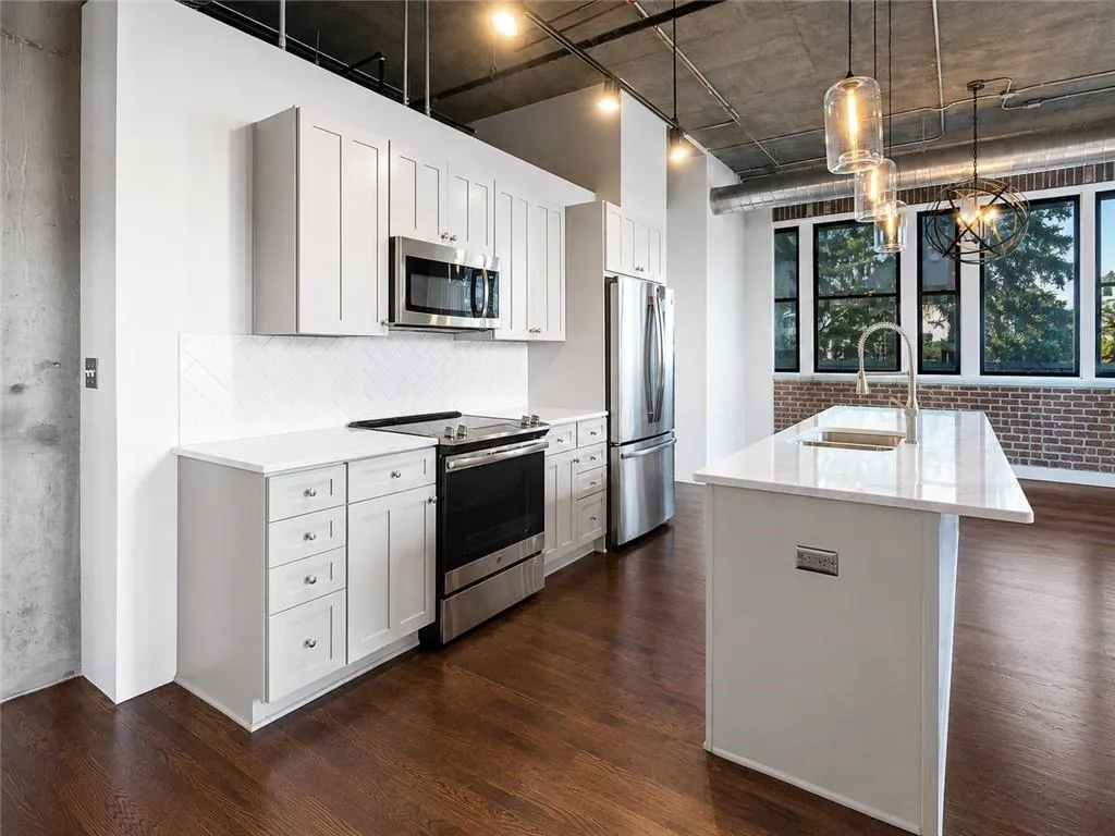 Kitchen featuring stainless steel appliances, white shaker cabinetry, an island with an undermount sink, and a herringbone-patterned backsplash