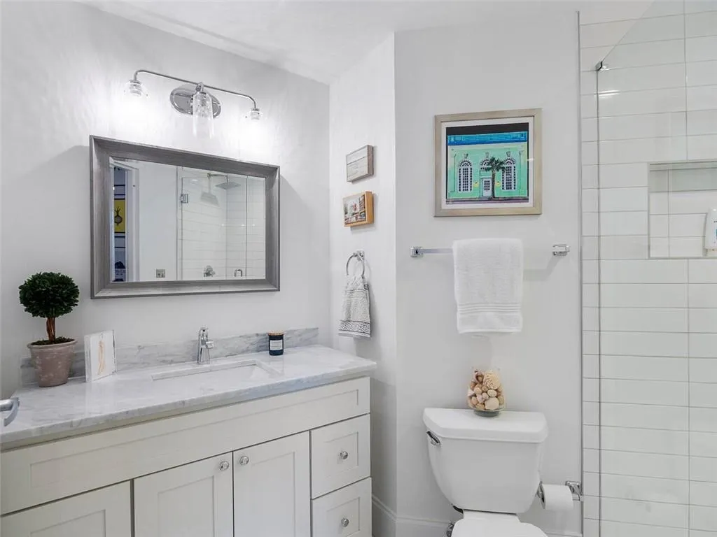 White vanity with stone countertop and integrated sink, framed mirror, and chrome light fixture