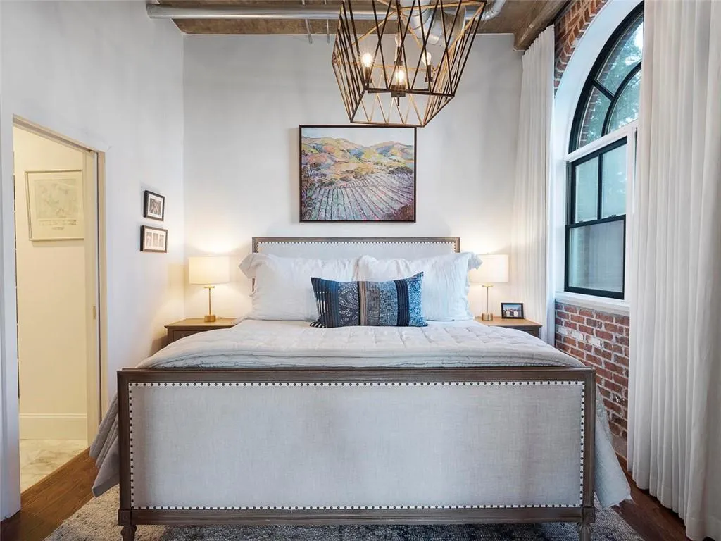 Exposed brick accent wall with an arched window, high ceilings, and wood-finish flooring