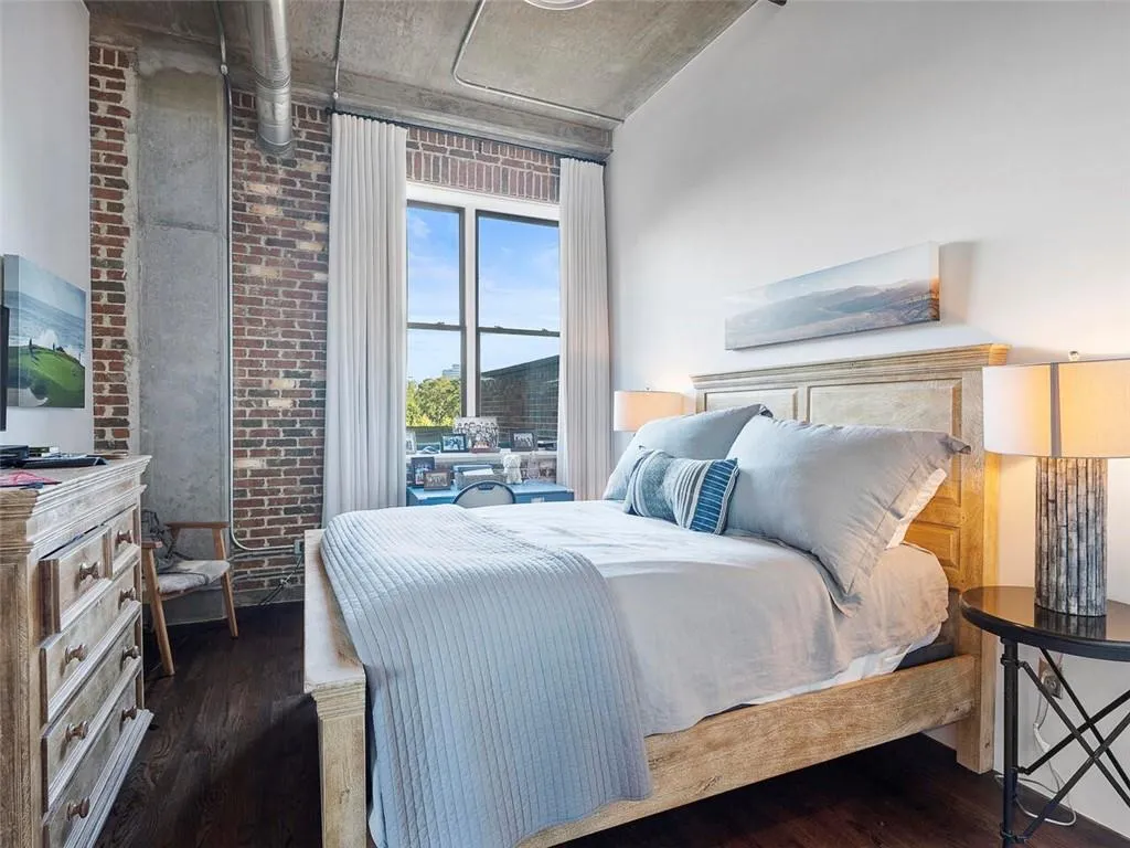 Exposed brick wall, concrete ceiling, dark wood-finish flooring, and large window with white drapery