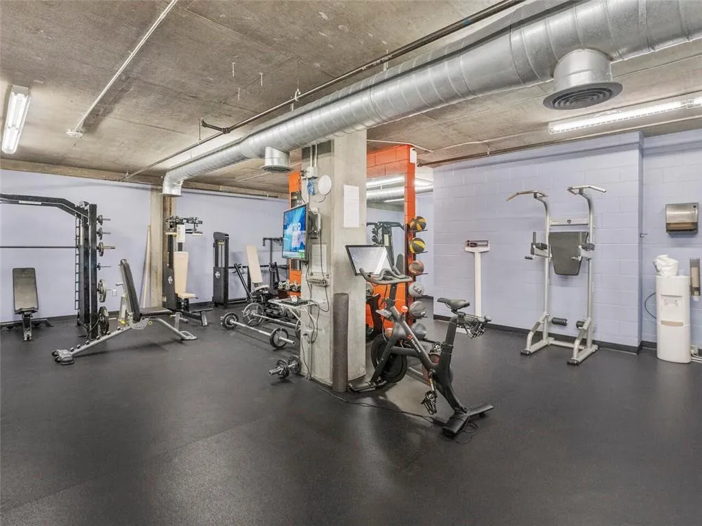 Fitness area featuring rubber flooring, exposed ductwork, and ceiling-mounted linear lighting
