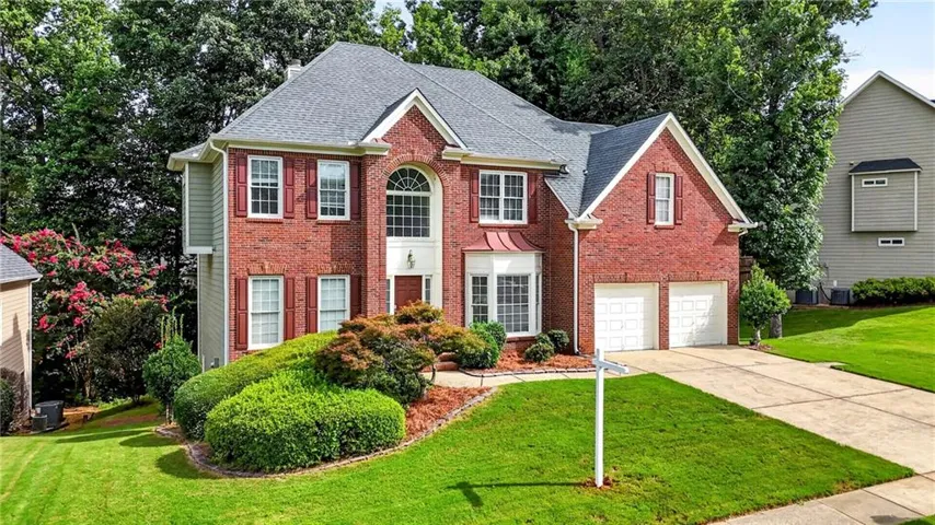 Traditional brick facade residence with a two-car garage, manicured front lawn, established landscaping, and a prominent arched window feature